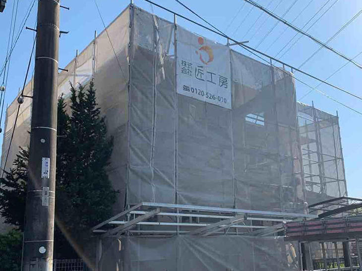足場を組立て、メッシュシートを張っています。屋根カバー工事と外壁塗装工事を行います。担当：中島凌太